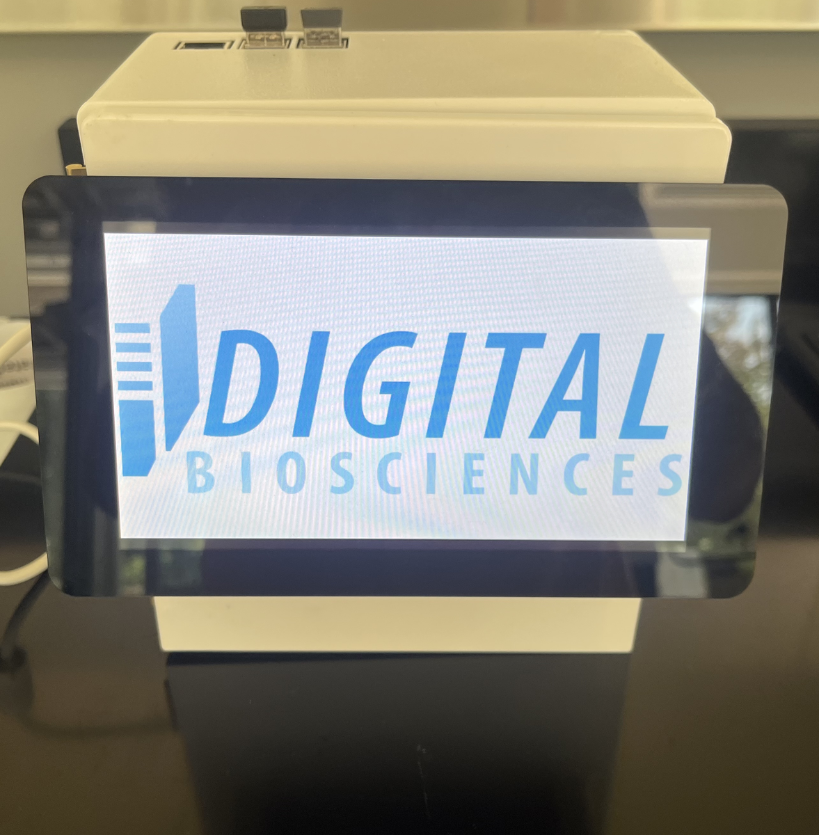 The SepsisDx reader on a bench, powered on, its screen showing the Digital Biosciences logo